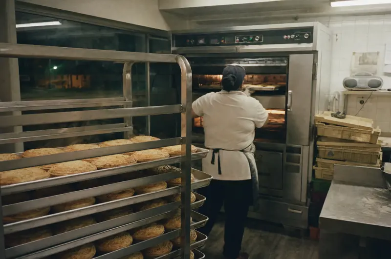 Racks of mince-and-cheese pies cooling at 5am in a small Papatoetoe bakery while the baker slides another tray into the deck oven