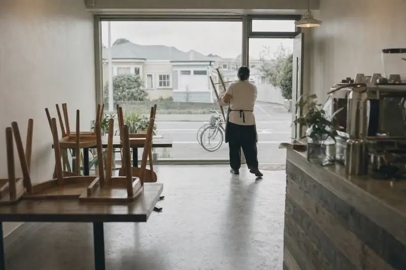 Before opening at a small café in Petone: chairs still upturned on the tables while the owner carries the first one toward the front window