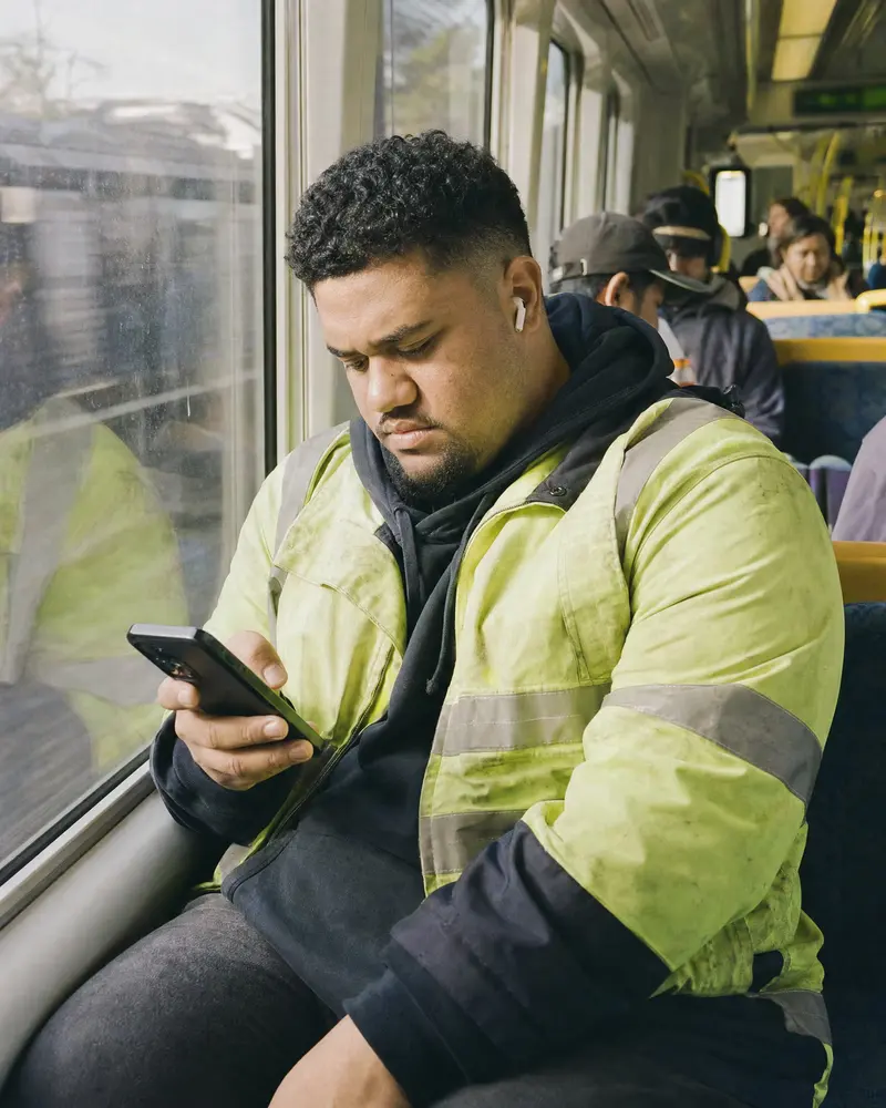 Young man in a hi-vis jacket working out numbers on his phone on an Auckland Southern Line train