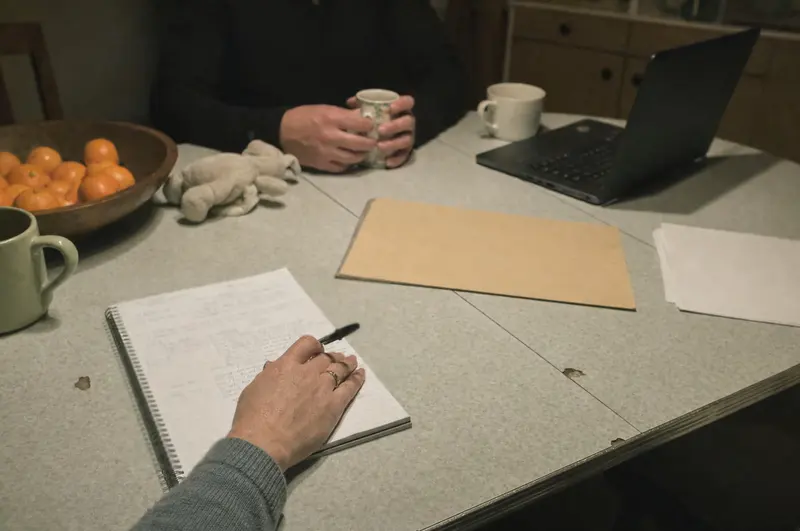 A mortgage adviser's handwritten notes on a kitchen table during an evening home visit in Palmerston North, a client's hands around a mug of tea across the table