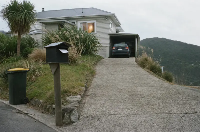 An envelope in the letterbox at the foot of a sloping driveway in Tawa, Wellington, the kitchen light on in the weatherboard house above